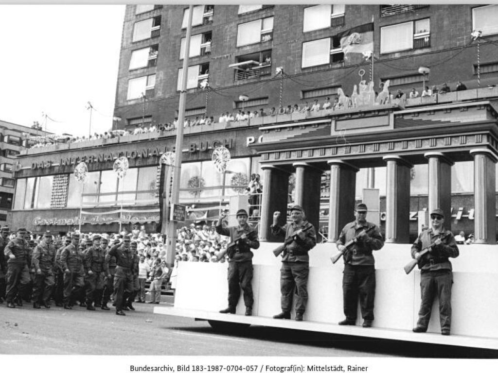 1987: Zur 750-Jahr-Feier in Ost-Berlin spielen Kampfgruppenmitglieder vor einer nachgebauten Kulisse die Errichtung des „antifaschistischen Schutzwalls“ nach. Interessanterweise stehen die Männer – anders als bei der Original-Aufnahme – auf der West-Berliner Seite des Brandenburger Tors und stellen sich bei dieser nachgestellten Szene mit ihren Waffen schützend vor die eigene Bevölkerung.