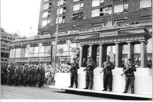 1987: Zur 750-Jahr-Feier in Ost-Berlin spielen Kampfgruppenmitglieder vor einer nachgebauten Kulisse die Errichtung des &bdquo;antifaschistischen Schutzwalls&ldquo; nach. Interessanterweise stehen die M&auml;nner &ndash; anders als bei der Original-Aufnahme &ndash; auf der West-Berliner Seite des Brandenburger Tors und stellen sich bei dieser nachgestellten Szene mit ihren Waffen sch&uuml;tzend vor die eigene Bev&ouml;lkerung.