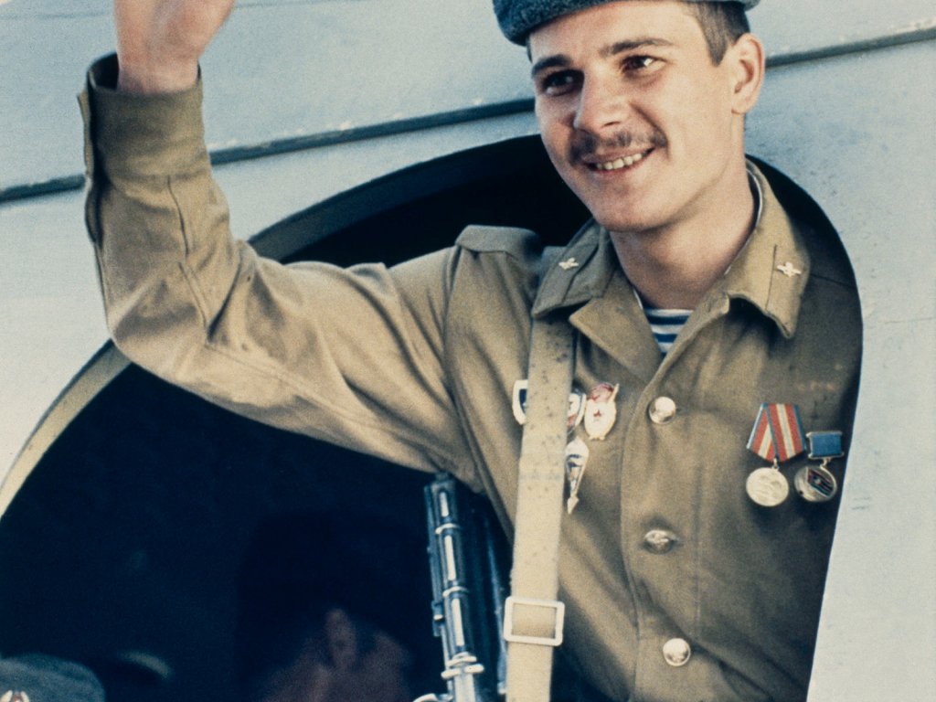 Ein sowjetischer Soldat steht lächelnd in der Tür eines Flugzeuges und hebt die rechte Hand zum Gruß.