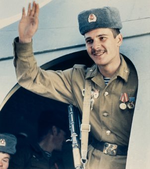 Ein sowjetischer Soldat steht lächelnd in der Tür eines Flugzeuges und hebt die rechte Hand zum Gruß.