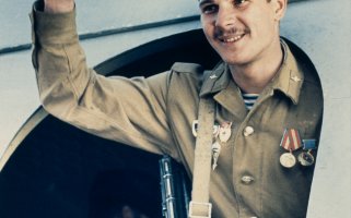 Ein sowjetischer Soldat steht lächelnd in der Tür eines Flugzeuges und hebt die rechte Hand zum Gruß.