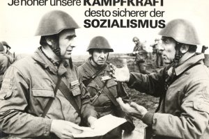 Drei uniformierte, bewaffnete Männer in Stahlhelmen diskutieren im Vordergrund. Im Hintergrund sind weitere Soldaten zu sehen. Das Bild ist beschriftet mit: Ja höher unsere Kampfkraft desto sicherer der Sozialismus.