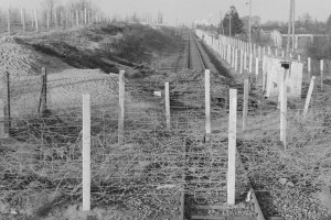 Quer über die Eisenbahnschienen verlaufen Stacheldrahtverhaue, dahinter liegt ein Haufen Schotter auf den Gleisen.