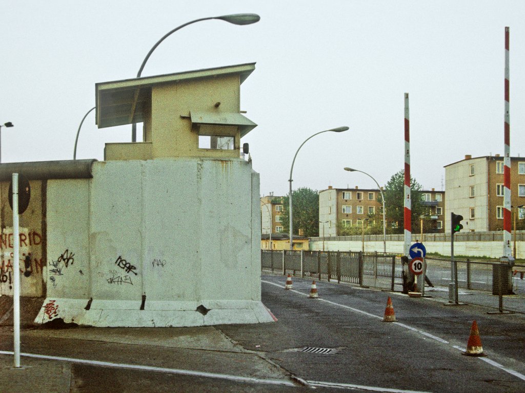 Blick von der Prinzenstraße in Kreuzberg (West-Berlin) auf den Grenzabfertigungsbereich in der Heinrich-Heine-Straße in Mitte (Ost-Berlin); Aufnahme 10. Mai 1990  Im Vordergrund links ist ein Stück Mauer zu sehen, das mit einem Wachturm abschließt. Rechts davon befinden sich die Grenzsicherungsanlagen der Übergangsstelle Heinrich Heine Straße, dahinter stehen drei Wohnblocks.
