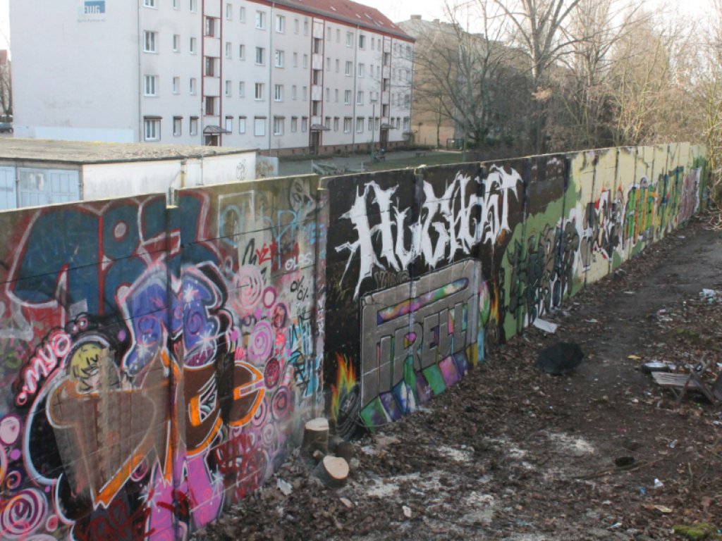 Das 60 Meter lange Teilstück der Hinterlandmauer stand bis März 2020 in Pankow nahe der Dolomitenstraße, 13. Februar 2020 Ein mit Graffiti buntbemaltes Stück der Hinterlandmauer zieht sich von vorne links nach hinten rechts durch das Bild. Hinter der Mauer stehen Wohnblöcke. Auf der Vorderseite liegt vereinzelt Müll auf dem Erdboden.