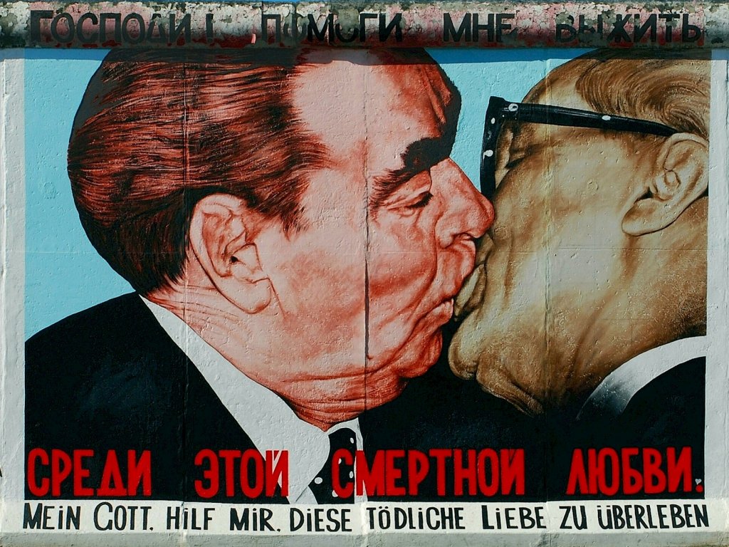 The picture shows the painting of the kissing politicians on the wall. The title of the artwork is in Russian and in German.