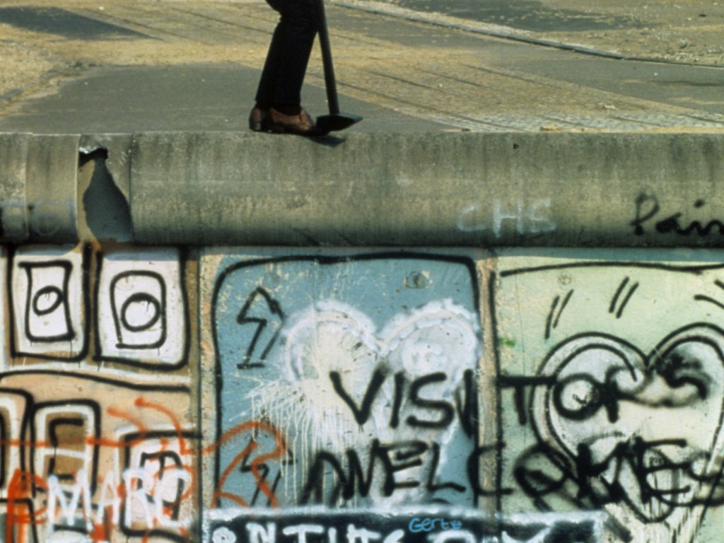 1986: In der Bundesrepublik ist die offizielle Kritik an der Berliner Mauer seit den 1970er Jahren leiser geworden. Die Mauer gleicht auf westlicher Seite mittlerweile einer riesigen Leinwand. Der kanadische Friedensaktivist John Runnings erregt mit seinem politischen Protest am 25. Jahrestag Aufmerksamkeit: er klettert auf die Mauerkrone und schlägt mit einem Hammer auf sie ein. DDR-Grenzsoldaten nehmen ihn schließlich fest, er verbringt drei Monate in Haft in Ost-Berlin.