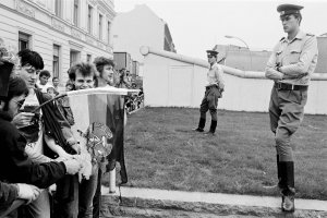 1989: Protestaktion zum 28. Jahrestag des Mauerbaus. West-Berliner Demonstranten verbrennen vor den Grenzsoldaten am Checkpoint Charlie eine DDR-Flagge.