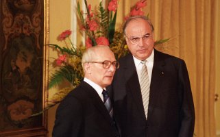 Honecker steht links neben Kohl. Im Hintergrund ein golden gerahmtes Bild und ein großer Blumenstrauß.
