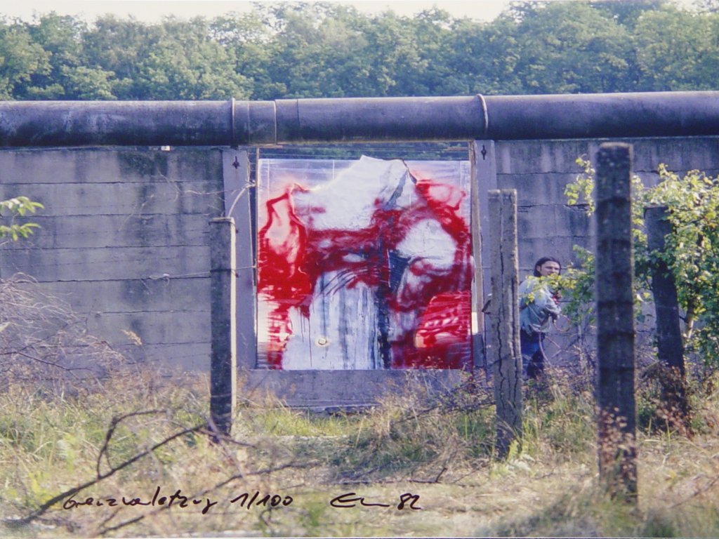 Die Mauer ist aus einigen Metern Entfernung frontal aufgenommen. Im Zentrum ist das abstrakte Bild in der Mauerlücke. Links neben dem Bild ist Stephan Elsner, der dabei ist, wegzulaufen.